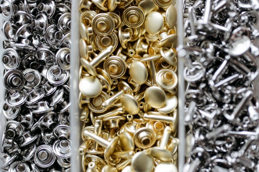 Close-up view of gold and silver metal studs organized in bins for crafting or manufacturing.