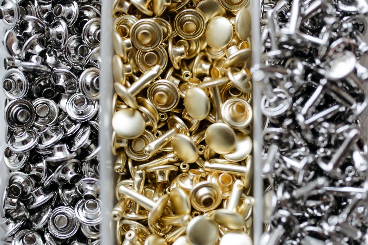 Close-up view of gold and silver metal studs organized in bins for crafting or manufacturing.
